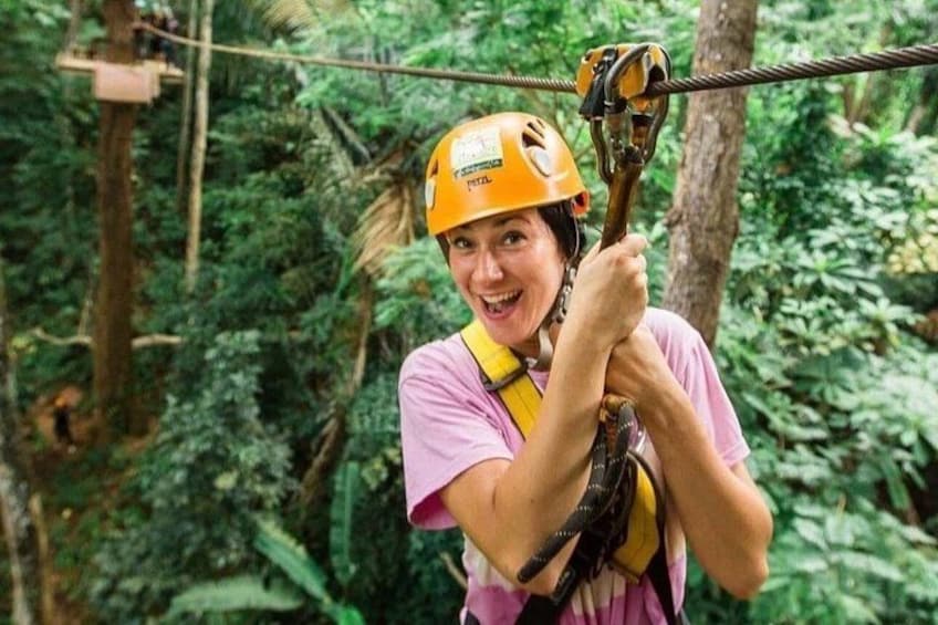A person in a forested area with a zip line, wearing a helmet and harness. 2