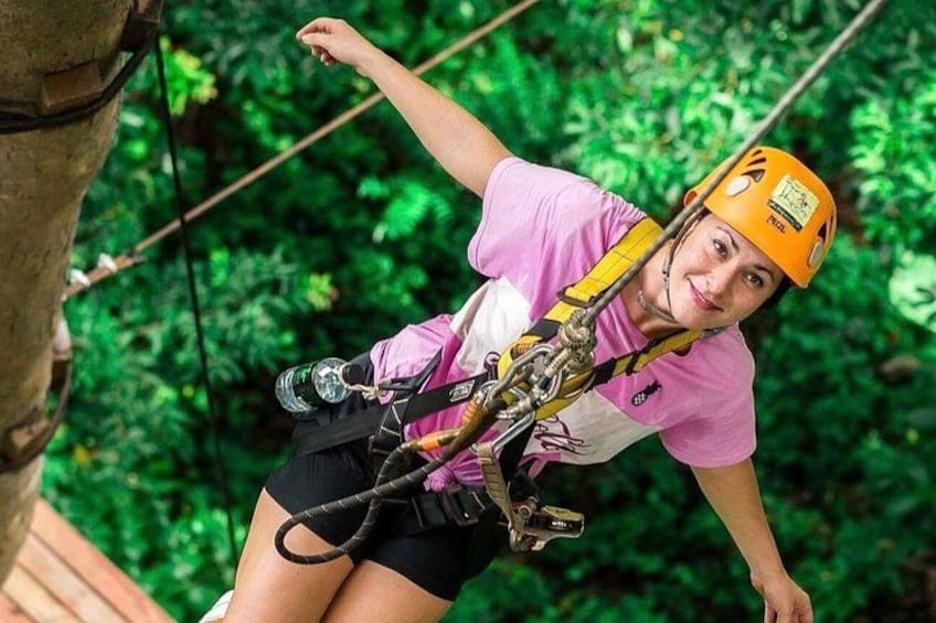 A person engaged in a zip-lining activity, wearing a helmet and harness, with dense green foliage in the background. 3