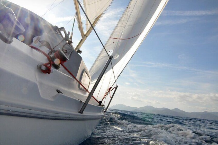 A sailboat with white sails and red rigging, moving through choppy waters with mountains in the background. 4
