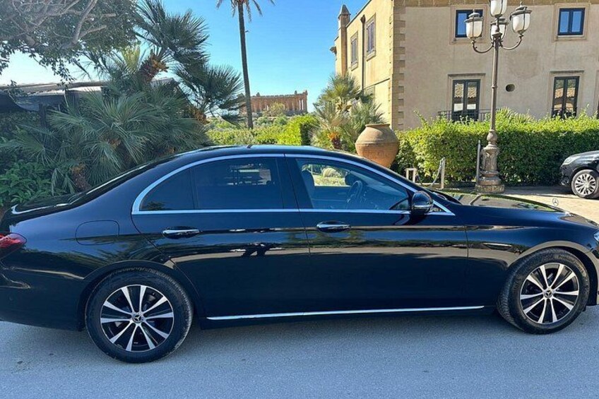 A black sedan parked on a street with a building and palm trees in the background. 2