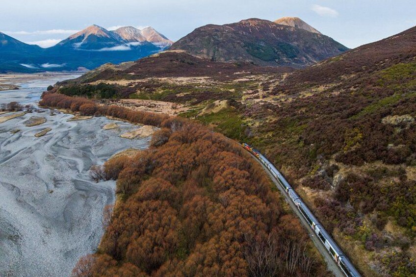 A train traveling through a mountainous landscape with a river and autumn-colored trees. 3