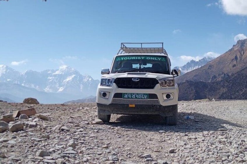 A white SUV with 'TOURIST ONLY' on the windshield, parked on a rocky terrain with mountains in the background. 2