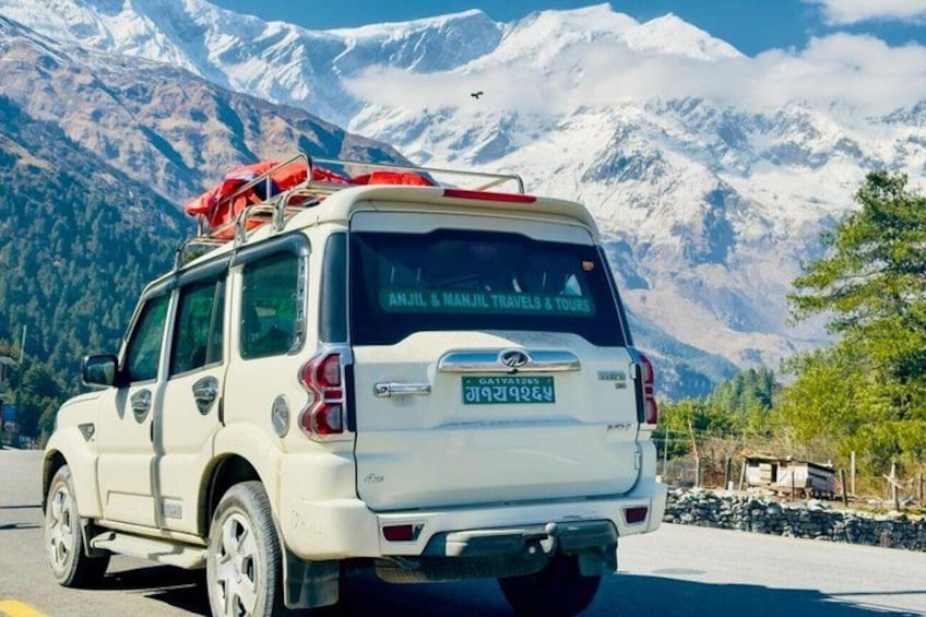 A white SUV with a red flag on top, parked on a road with snow-capped mountains in the background. 2