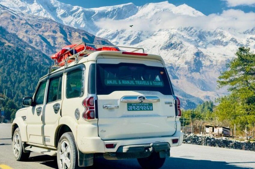 A white SUV with a red flag on the roof, parked on a road with snow-capped mountains in the background. 4