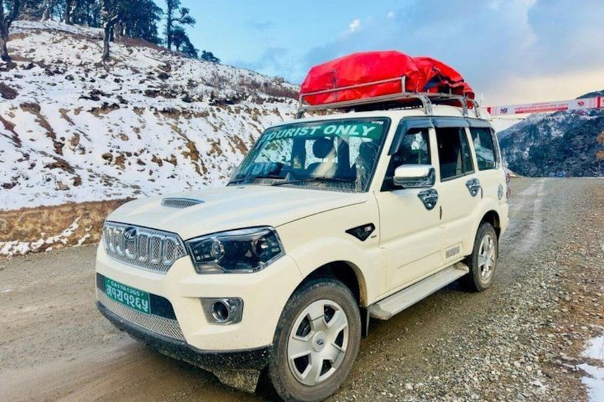A white SUV with a red cover on the roof, parked on a snowy road with a mountainous landscape in the background. 3