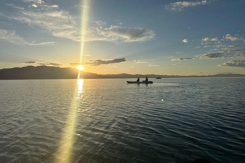 Un lac paisible sur lequel navigue un bateau transportant deux personnes, un ciel dégagé et des montagnes à l’horizon. 4