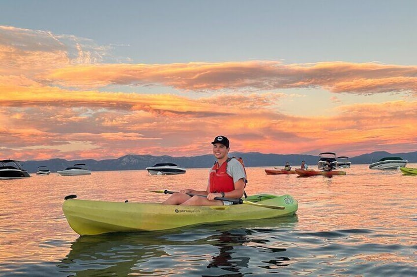 Una persona practica kayak en aguas tranquilas durante el atardecer, con varias embarcaciones al fondo. 1