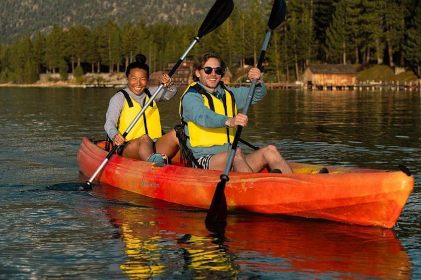 Two people kayaking on a calm lake surrounded by trees. 2