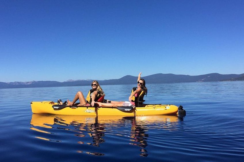 Two people in a yellow kayak on calm water with mountains in the background. 3