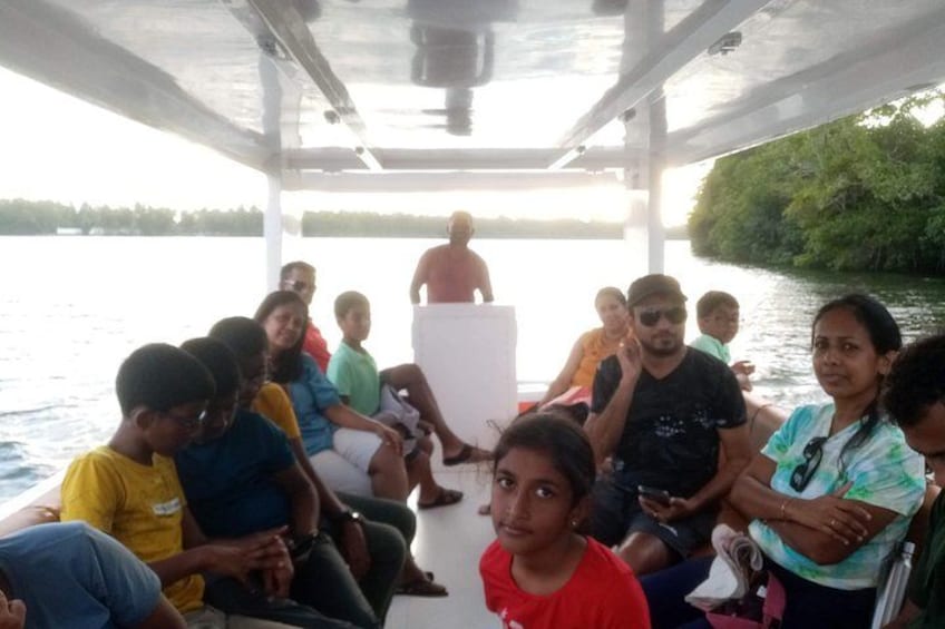 A group of people on a boat with a calm water body and greenery in the background. 1