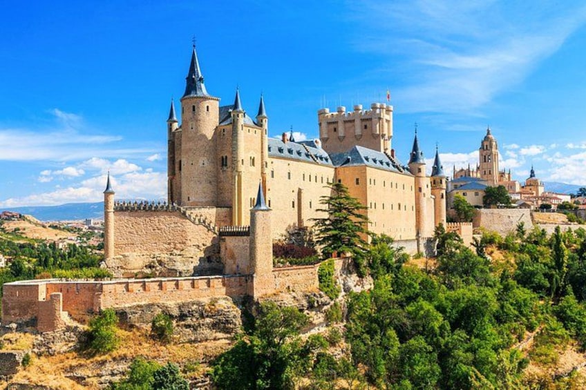 Un castillo histórico con múltiples torres, rodeado por una muralla fortificada y abundante vegetación. 5