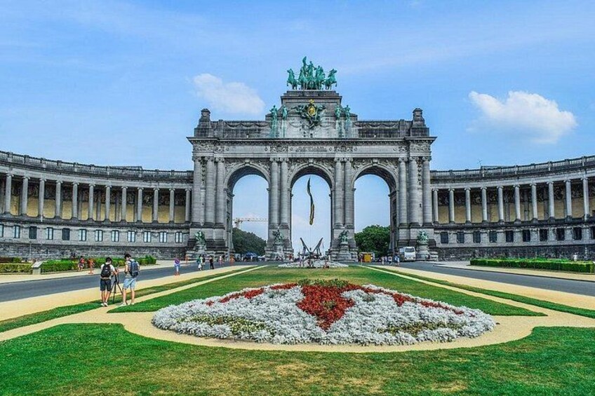 Un'ampia e decorata arcata con statue sulla sommità, circondata da un giardino curato con fiori rossi. 5