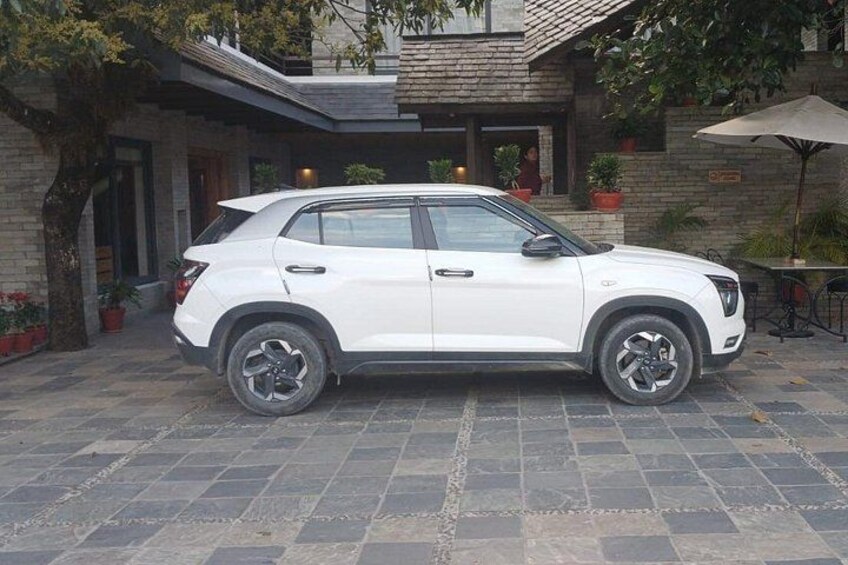 Un SUV blanco estacionado en un camino de entrada con un patio de piedra, una casa de ladrillo y plantas en macetas. 2