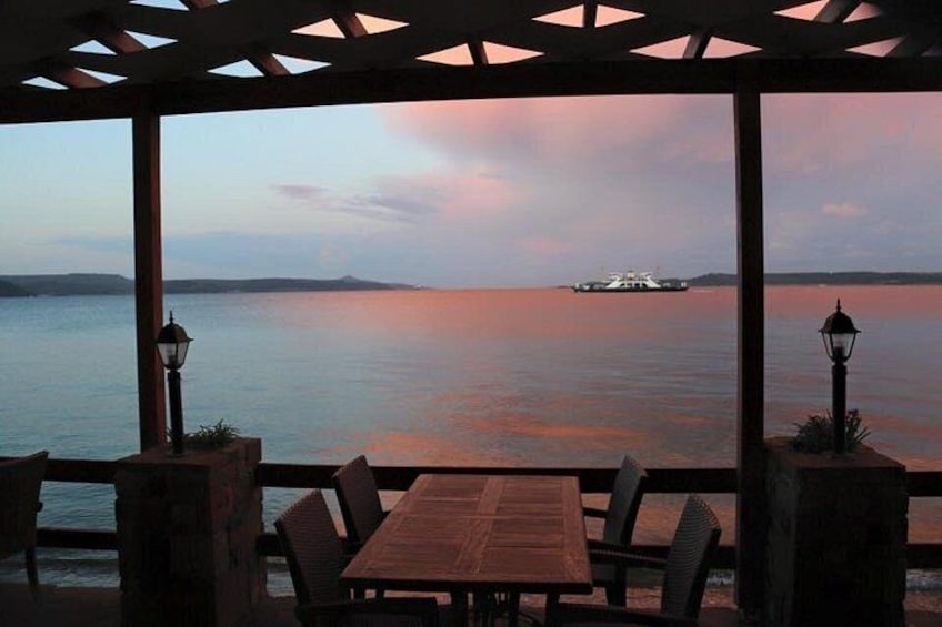 A wooden table and chairs under a pergola overlooking a body of water with a boat in the distance. 2