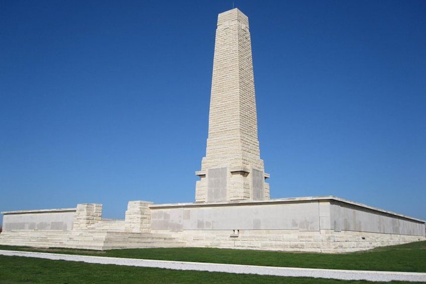 A tall, narrow monument with a stepped base, surrounded by a flat, grassy area. 1