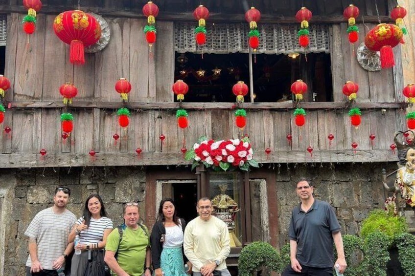 En grupp människor som står framför en traditionell byggnad med röda lyktor och blomsterdekorationer. 2