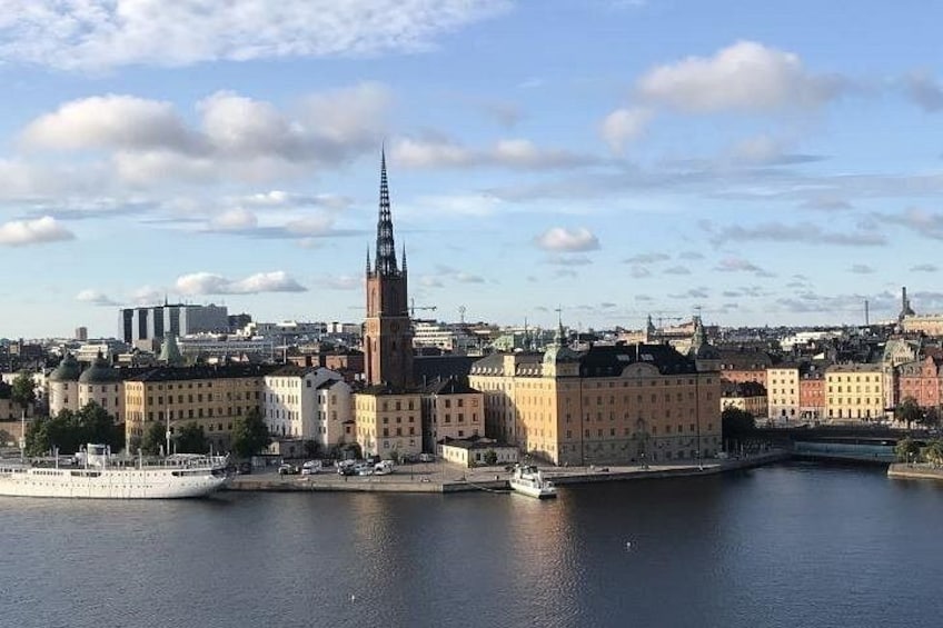 Et bybillede med et markant kirketårn, en havnefront og flere bygninger langs floden. 3
