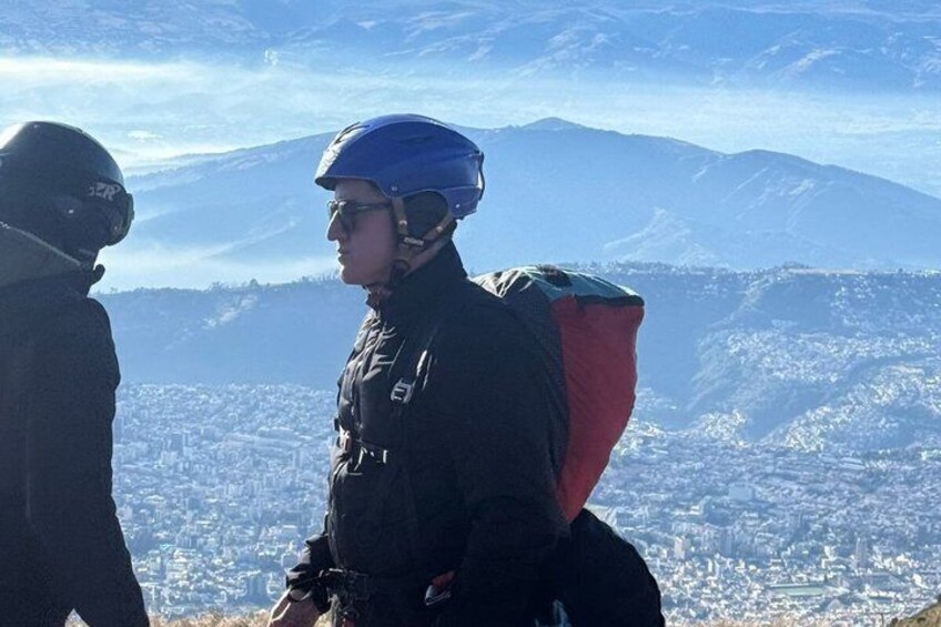 Dos personas con casco y mochilas en una montaña, con un paisaje urbano al fondo. 3