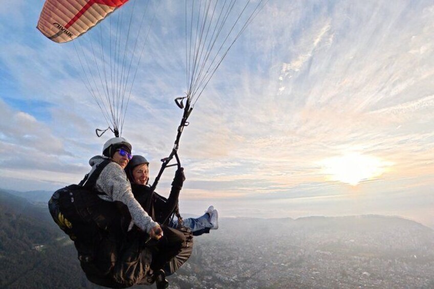 Dos personas practicando parapente sobre un paisaje montañoso con el sol poniéndose al fondo. 2