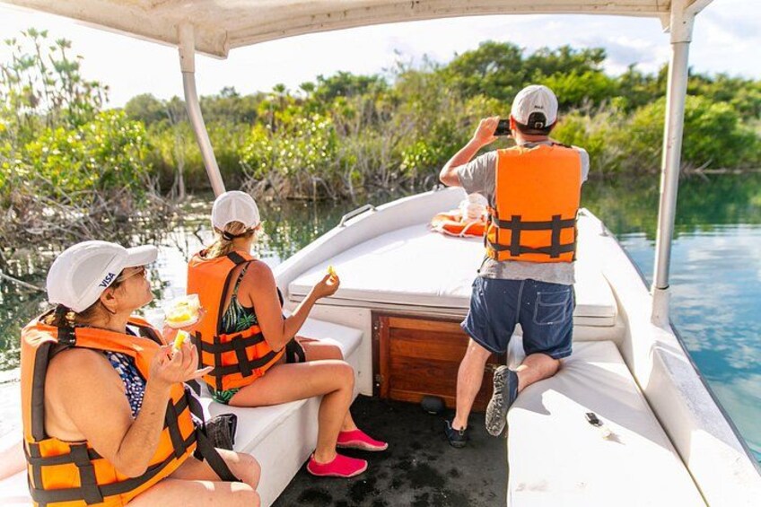 Three people on a boat wearing life jackets, surrounded by water and greenery. 1