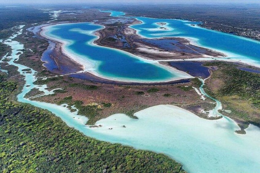 An aerial view of a coastal area with multiple turquoise lagoons, surrounded by dense green vegetation and sandy beaches. 2