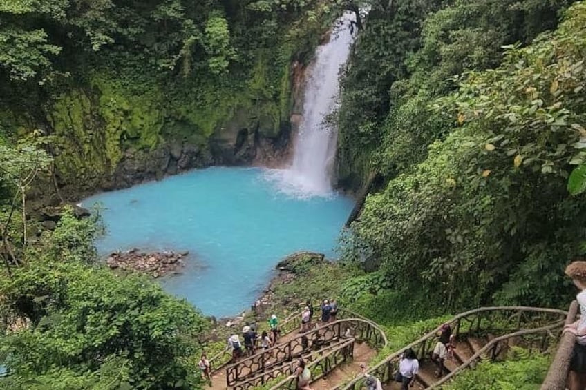 A waterfall, a turquoise pool, and a wooden staircase. 1