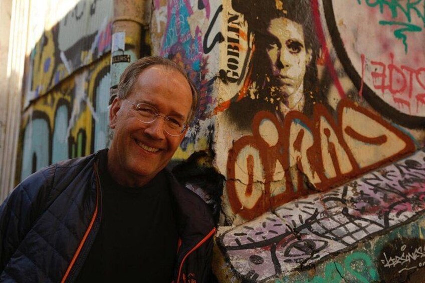 En mand står foran en væg med graffiti, hvor ordet 'O'RAS' er malet. 4