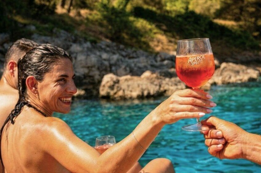 Two people toasting with a glass of red beverage by a body of water with rocky terrain in the background. 4