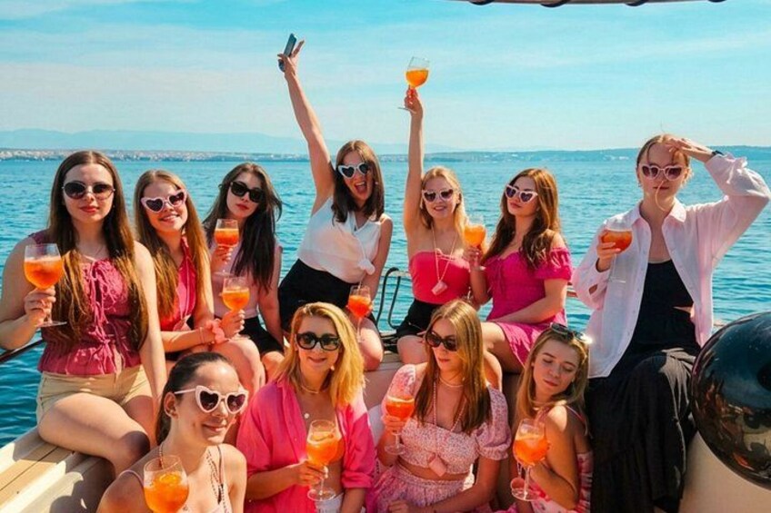 A group of people on a boat with drinks, a clear sky, and water in the background. 1
