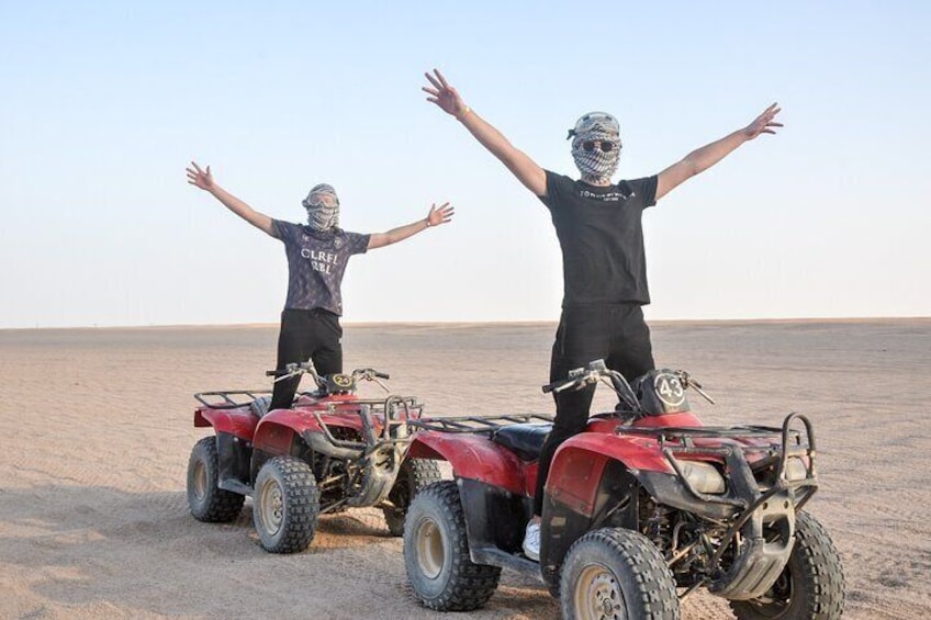Two people on ATVs in a desert with their arms outstretched. 5