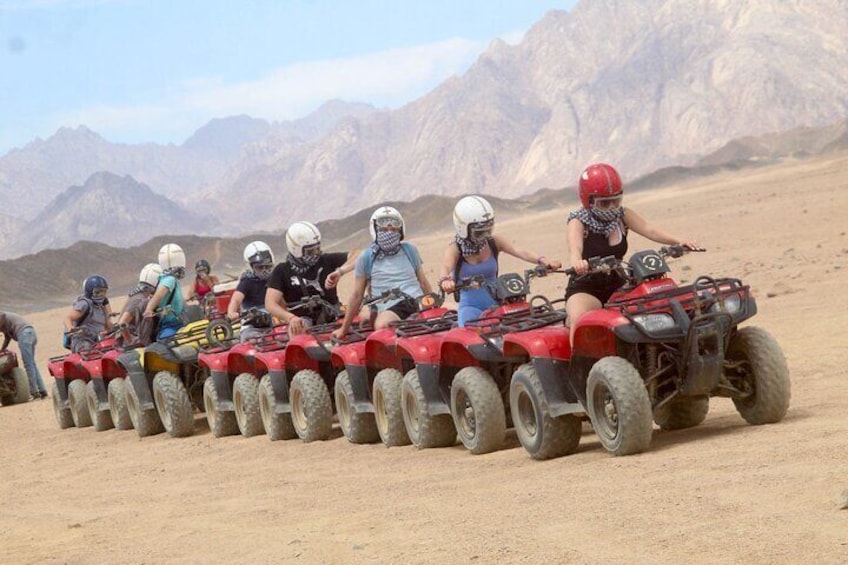 A group of people riding ATVs in a desert landscape with mountains in the background. 2