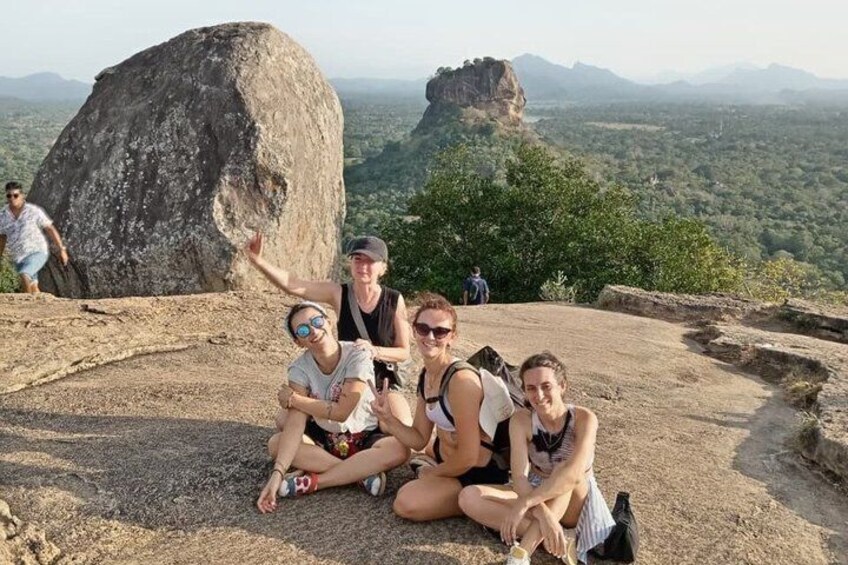 A group of people sitting on a rocky outcrop with a large rock formation and a view of the landscape in the background. 1