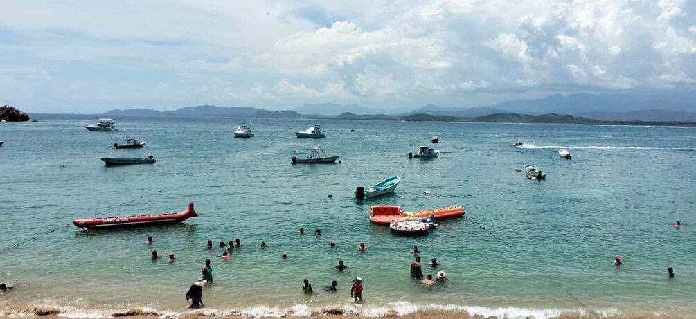 A coastal scene with numerous boats and people swimming in the water. 2
