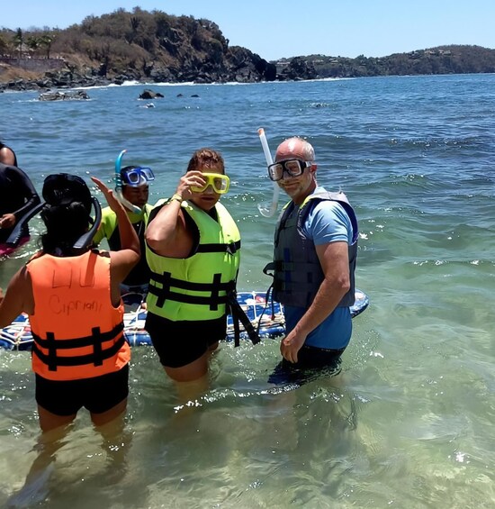 People in water with life vests and snorkels, a boat, and rocky cliffs in the background. 5