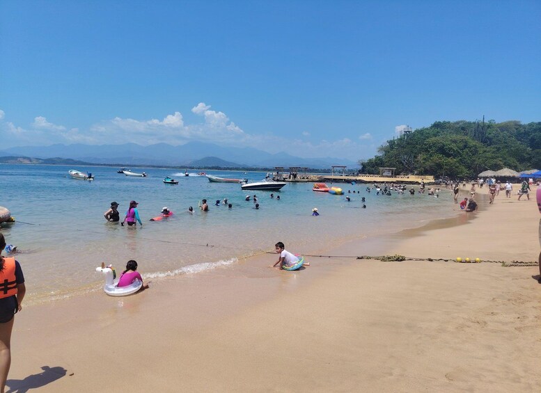 A beach with people swimming and boats in the water. 1