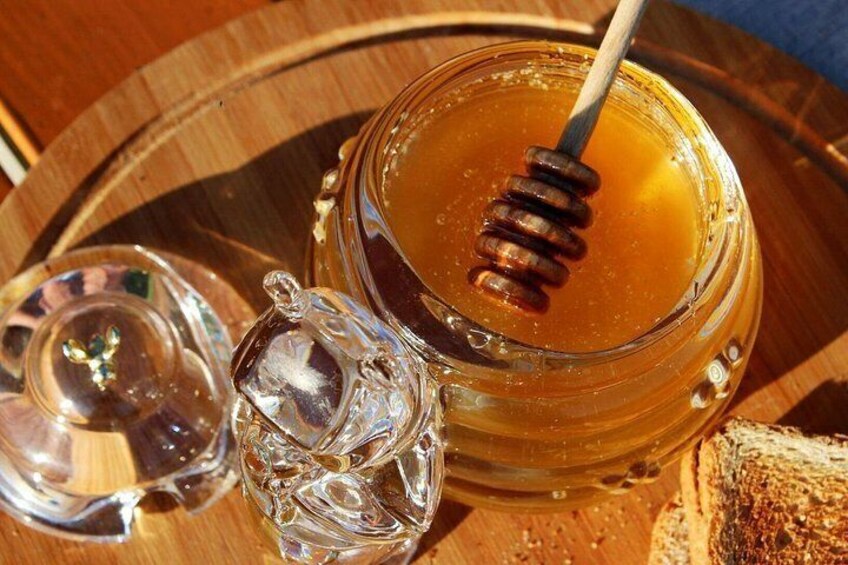 Un bocal en verre rempli de miel, accompagné d’une cuillère à miel, un verre d’eau et une tranche de pain, le tout posé sur un plateau en bois. 4