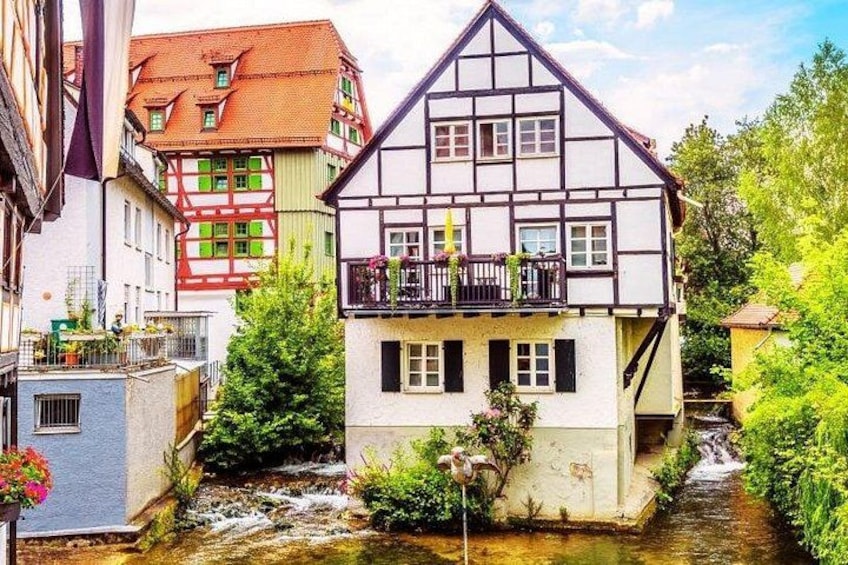 A traditional half-timbered house with a balcony, a small stream, and lush greenery. 3