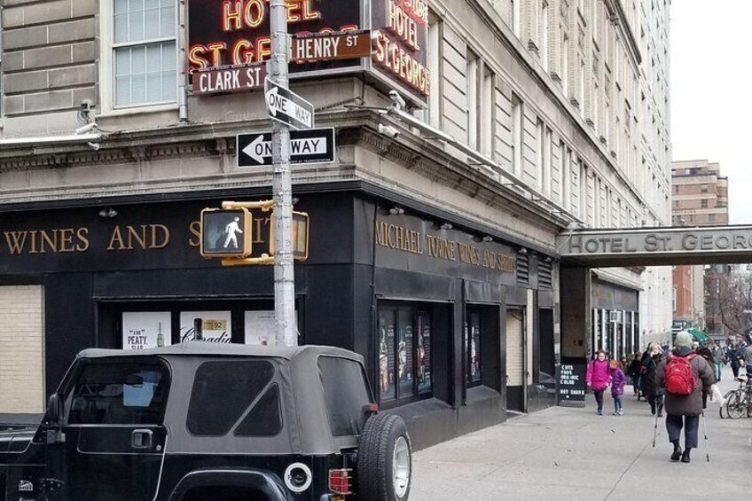 A street corner with a vintage car, a pedestrian crossing, and a building with a sign for Hotel St. George. 4
