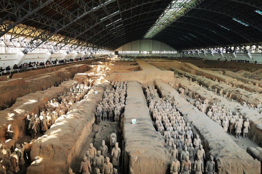 A large archaeological site with numerous terracotta soldier figures arranged in rows. 5