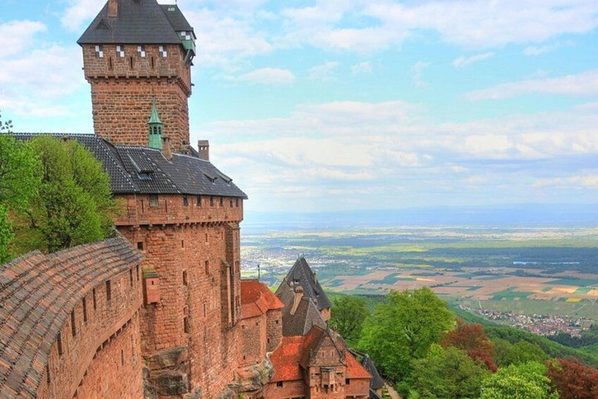A historic castle with a prominent tower, surrounded by lush greenery and a panoramic view of the countryside. 1