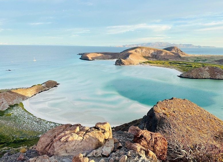 A coastal landscape with clear turquoise waters, rocky formations, and distant mountains. 1