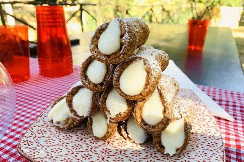 Een torentje van cannoli op een bord met een patroon, met rode bekers en een geruit tafelkleed op de achtergrond. 4