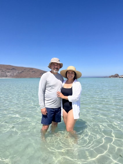 Un couple se tient dans une eau claire et peu profonde, avec un paysage montagneux en arrière-plan. 2