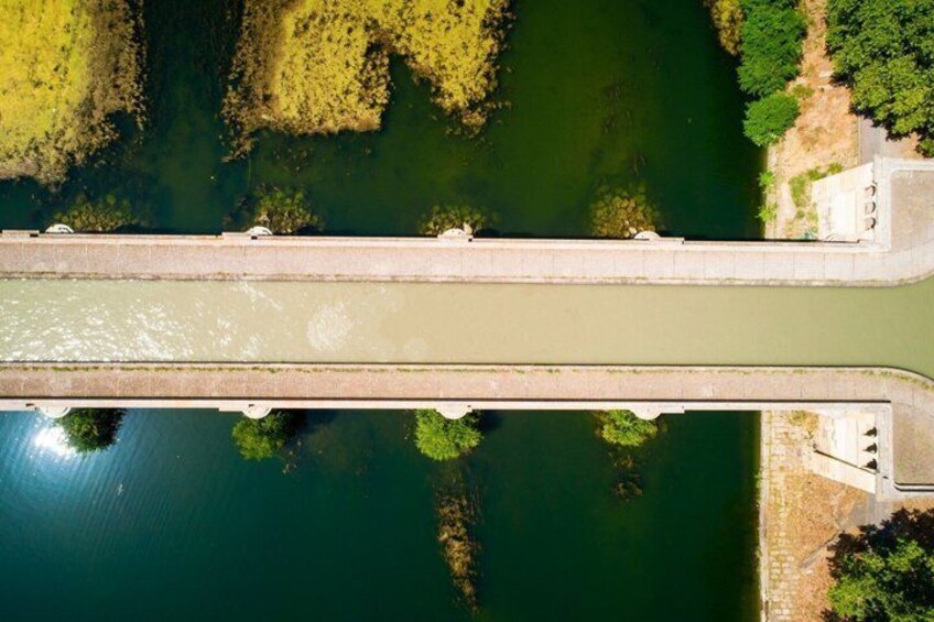 An aerial view of a bridge over a river with surrounding greenery and a small building on the right. 2