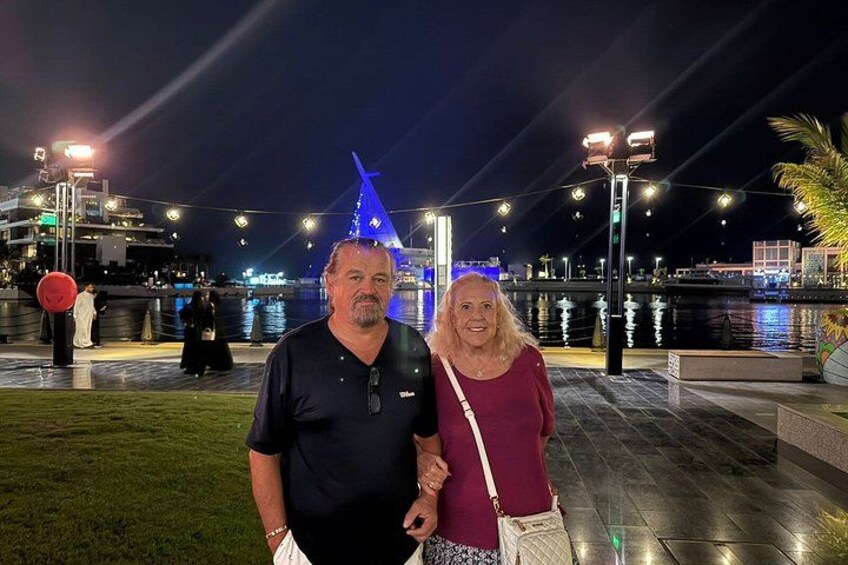 Two people standing in an outdoor area with a water body and illuminated structures in the background. 5