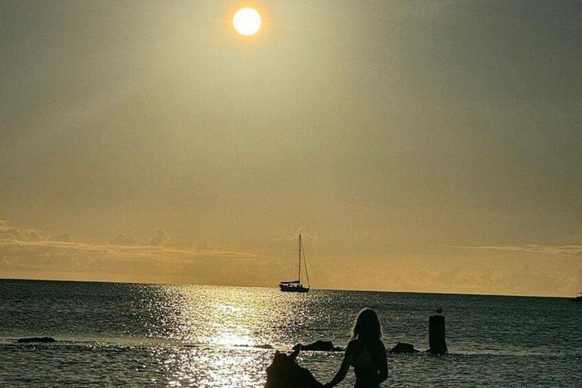 Un atardecer sobre un mar tranquilo con un velero y una persona cerca de la orilla. 4