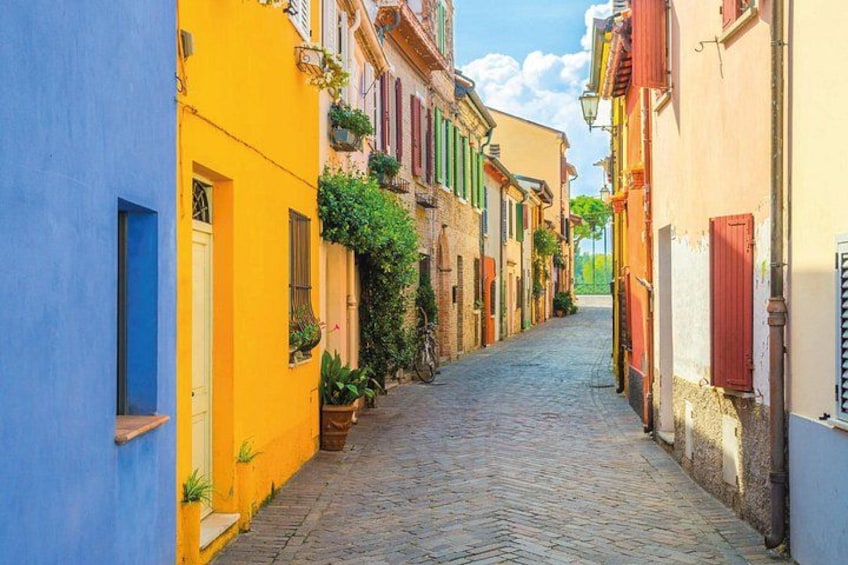 A narrow cobblestone street flanked by colorful buildings with shutters and balconies. 3