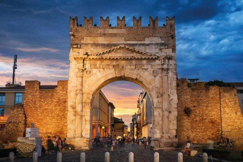 A stone archway with battlements, a cobblestone street, and a sunset in the background. 2