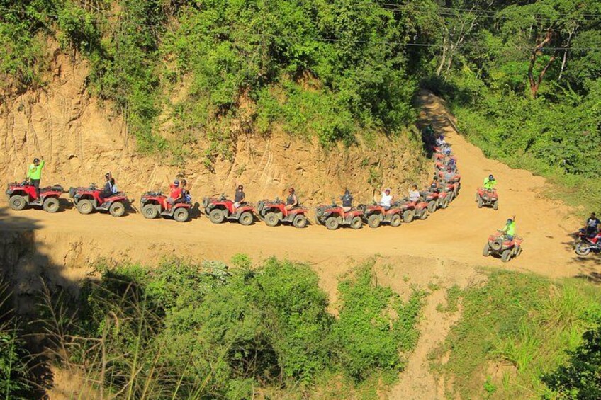 A line of red all-terrain vehicles on a dirt road surrounded by greenery. 4
