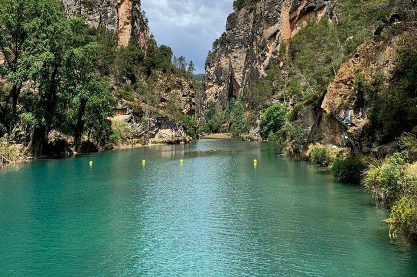 A river with clear turquoise water, surrounded by rocky cliffs and dense greenery. 5
